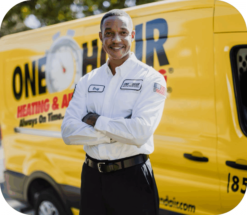 Smiling service technician wearing a white branded uniform, standing with arms crossed in front of a yellow heating and air service van