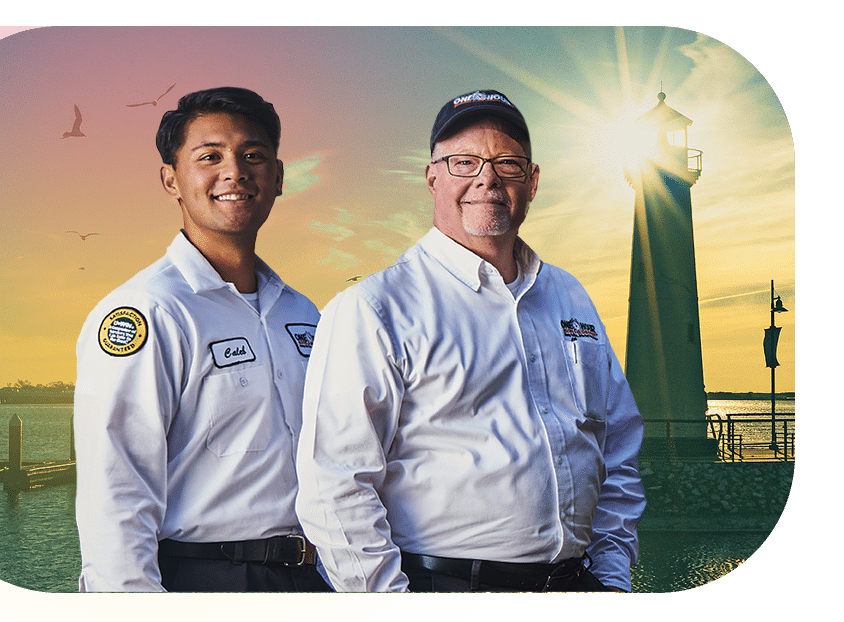 Two uniformed home service technicians standing together near a waterfront lighthouse at sunset.