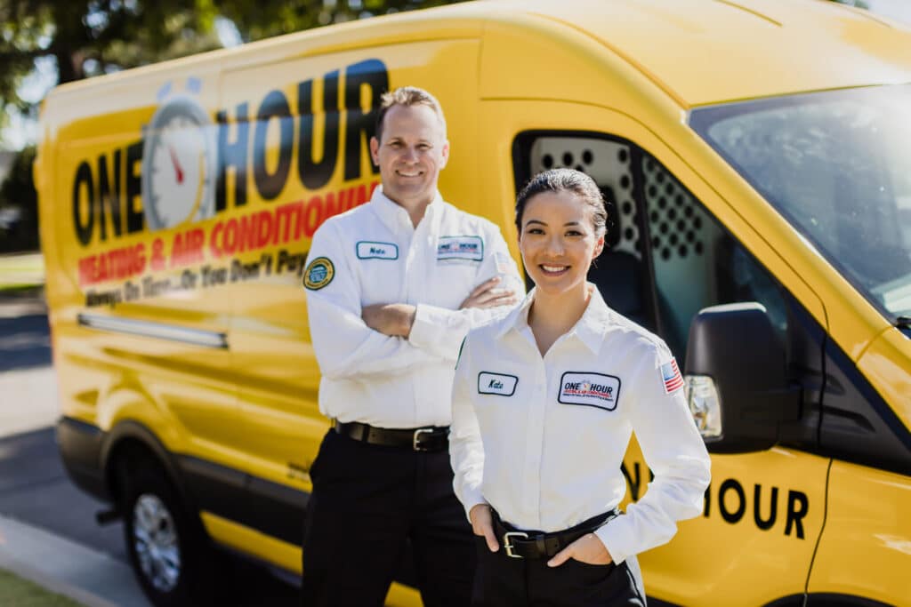 Two One Hour Air Conditioning & Heating technicians standing in front of a branded service van outdoors
