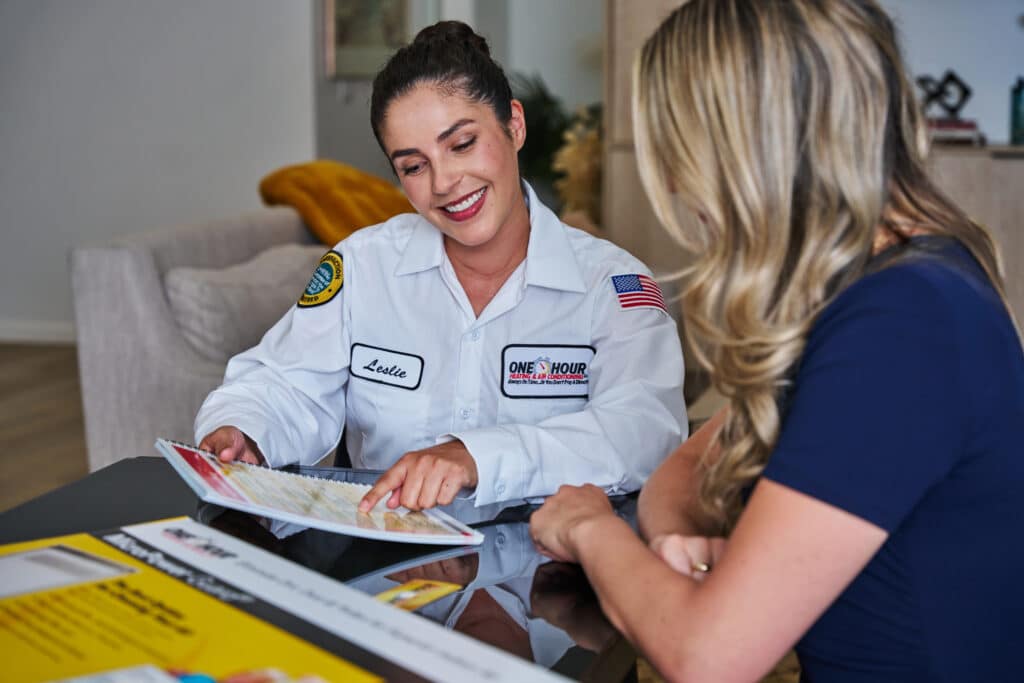 One Hour Air Conditioning & Heating technician reviewing service options with a homeowner at a kitchen table