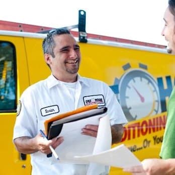 One Hour Air Conditioning & Heating technician reviewing paperwork with a homeowner beside a branded service vehicle